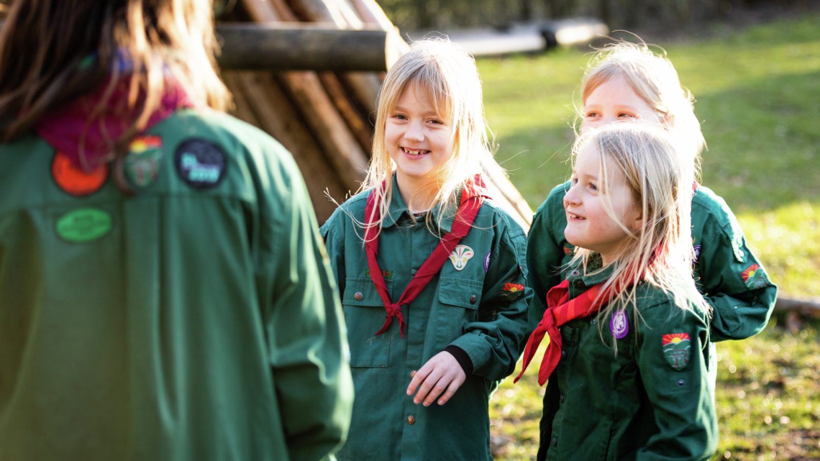 Piger i grønne spejderuniformer taler og griner med en voksen