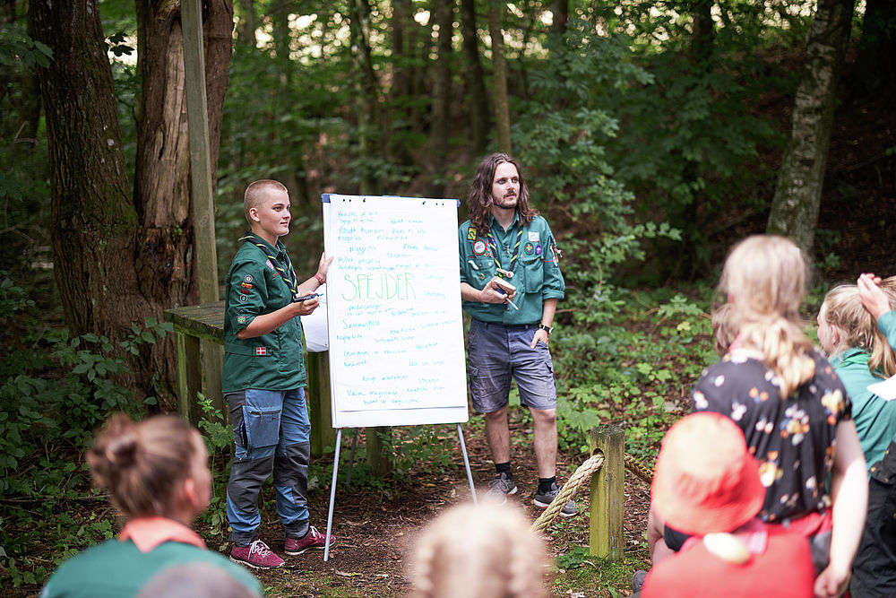 To spejderledere viser en færdselstavle for en gruppe børn