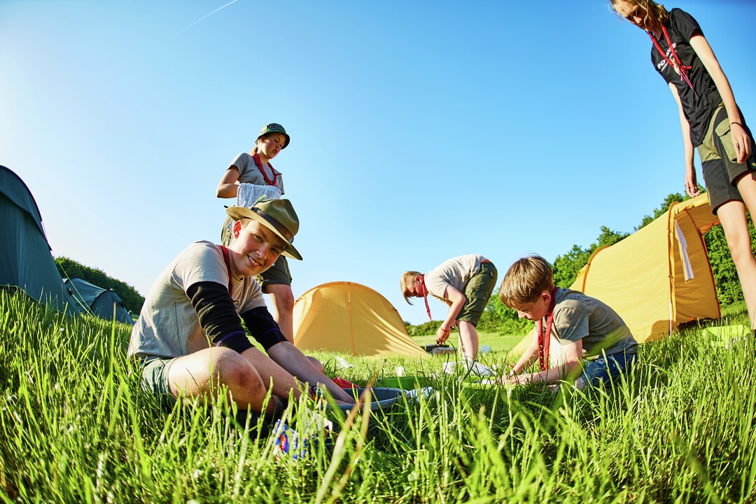 En dreng sidder i græsset med andre børn omgivet af telte.