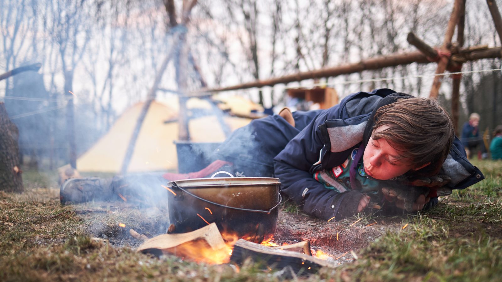 Dreng puster til flammerne i et bål