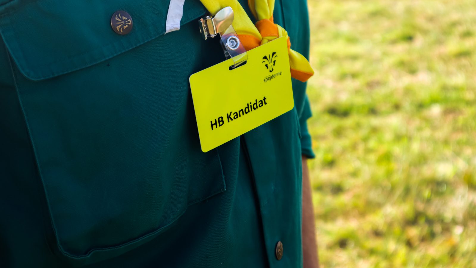 Navneskilt med teksten HB kandidat, der hænger i et spejdertørklæde.