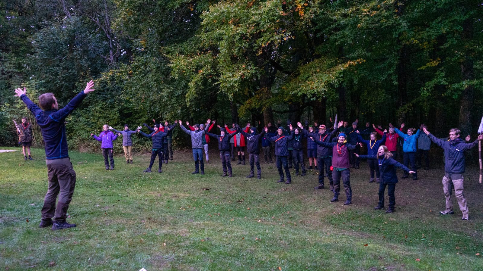 Spejdere står udenfor i en rundkreds med armene oppe