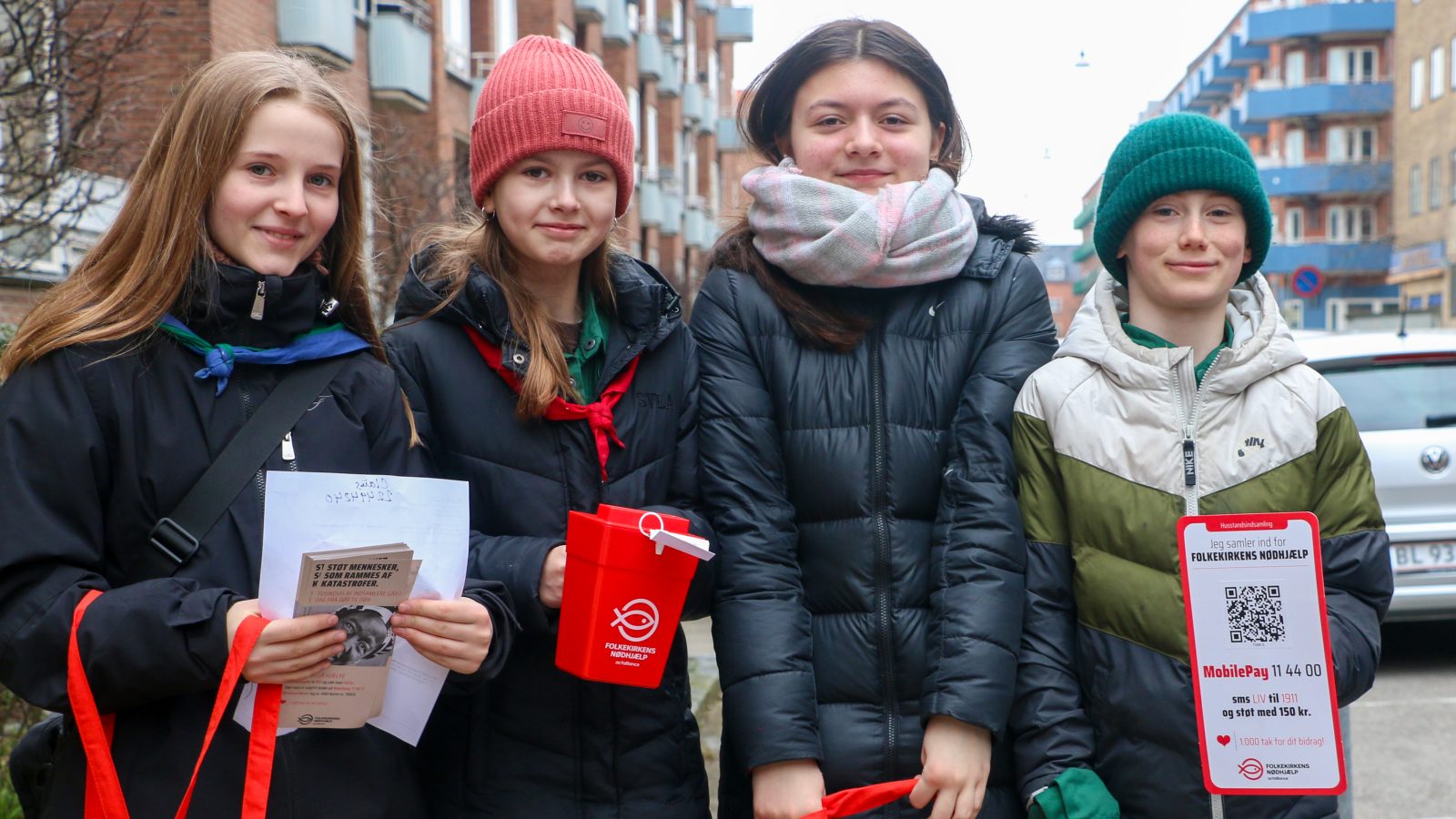 Fire spejdere i vinterjakker står med indsamlingsmaterialer til sogneindsamling Folkekirkens Nødhjælp