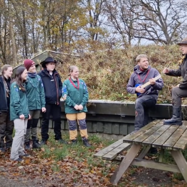 To spejderledere viser en færdselstavle for en gruppe børn